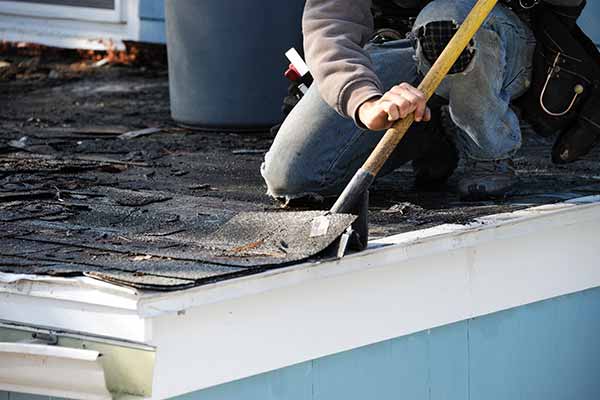 Worker removing dirty old shingles from a residential roof
